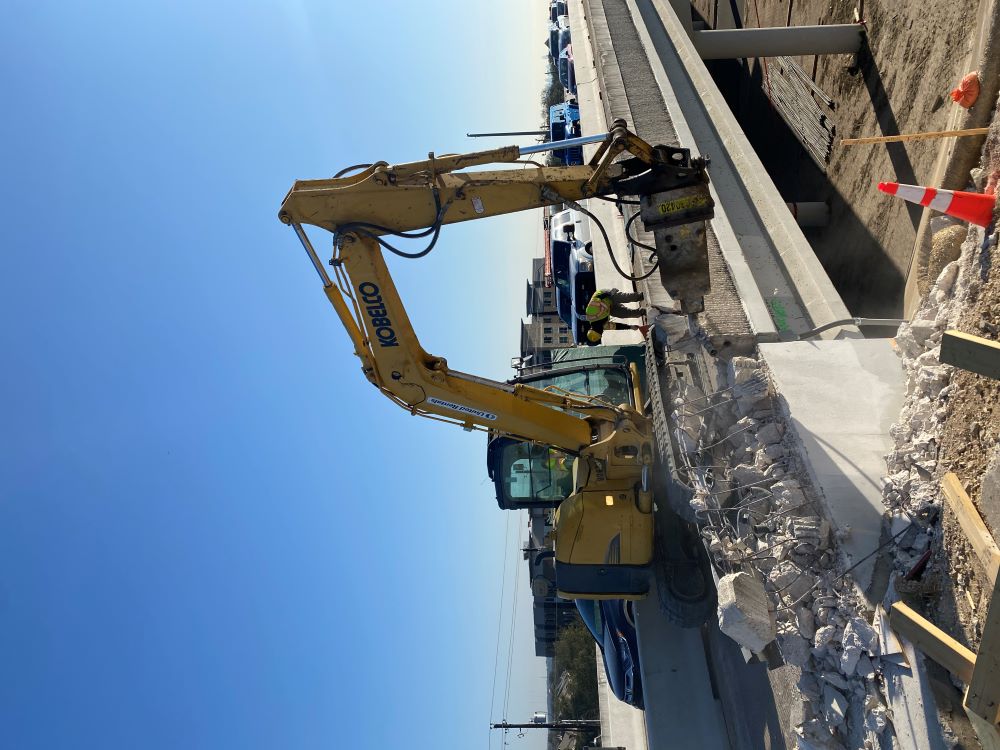 An excavator with a hammering attachment chips away at the barrier for the US 290 overpass bridge at Old Fredericksburg Road. This removal work is the first step of widening this bridge to add additional lanes in each direction.  March 2022