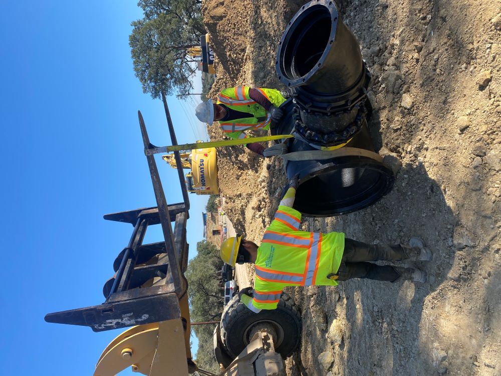 Oak Hill Parkway team members guide a forklift during placement of a water line fitting into a trench near Circle Drive. This curved fitting will connect a 30-inch water transmission line to smaller 16-inch distribution lines. January 2022