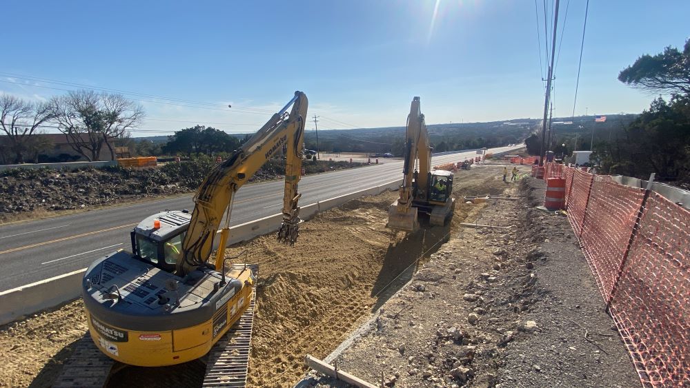 Looking west down US 290, two excavators work in tandem near the entrance to Alister Oak Hill apartments. In this location, US 290 will feature a widened center median and westbound deceleration lane for improved driver safety. March 2022