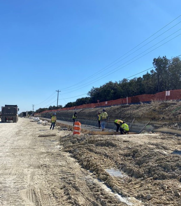 Oak Hill Parkway team members build a retaining wall near US 290 and RM 1826. A temporary orange construction fence runs adjacent to the TxDOT right-of-way line and keeps private properties separated from the active work areas below. February 2022   